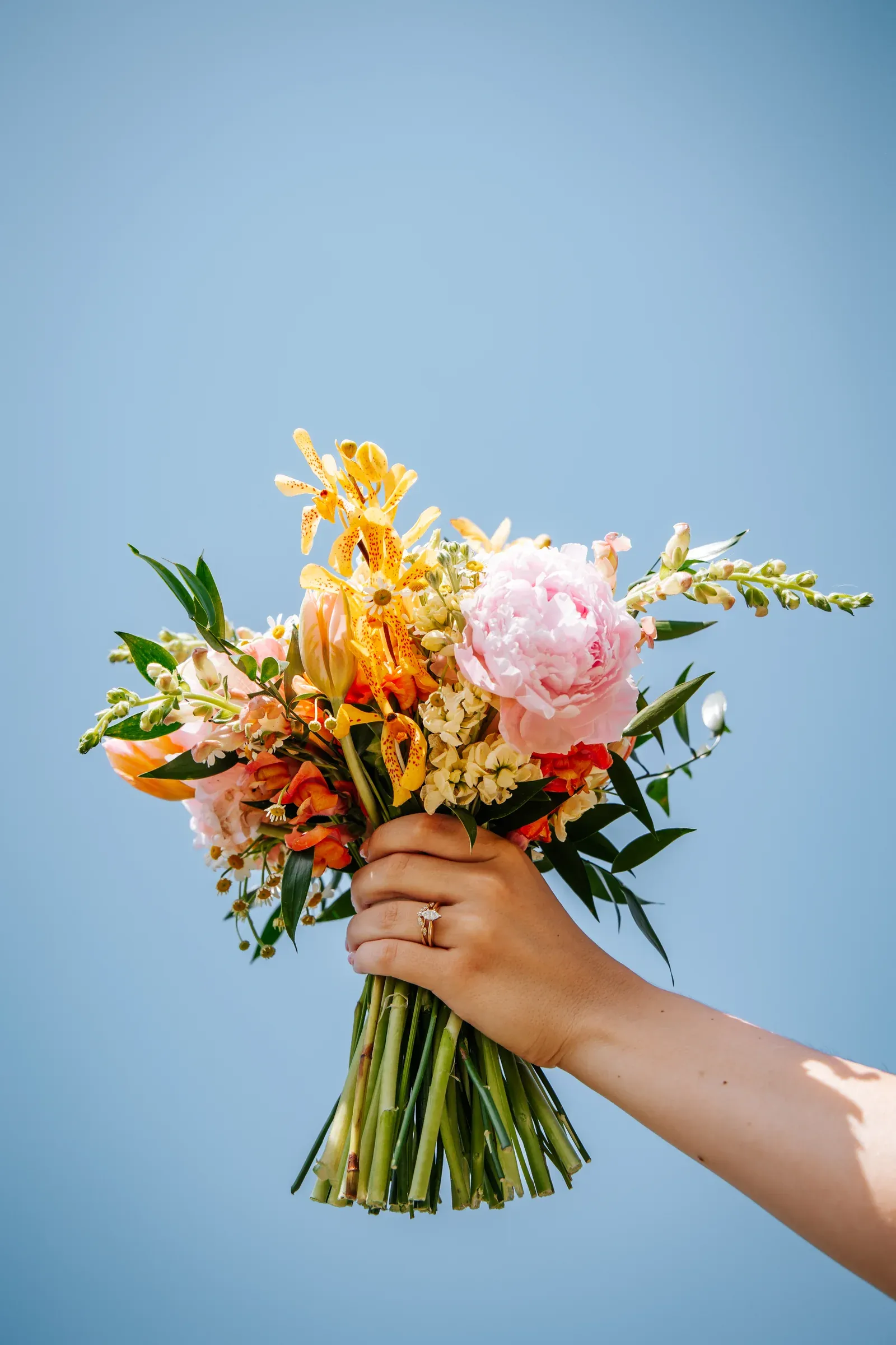 A bright orange and pink wedding bouquet held against a clear blue sky