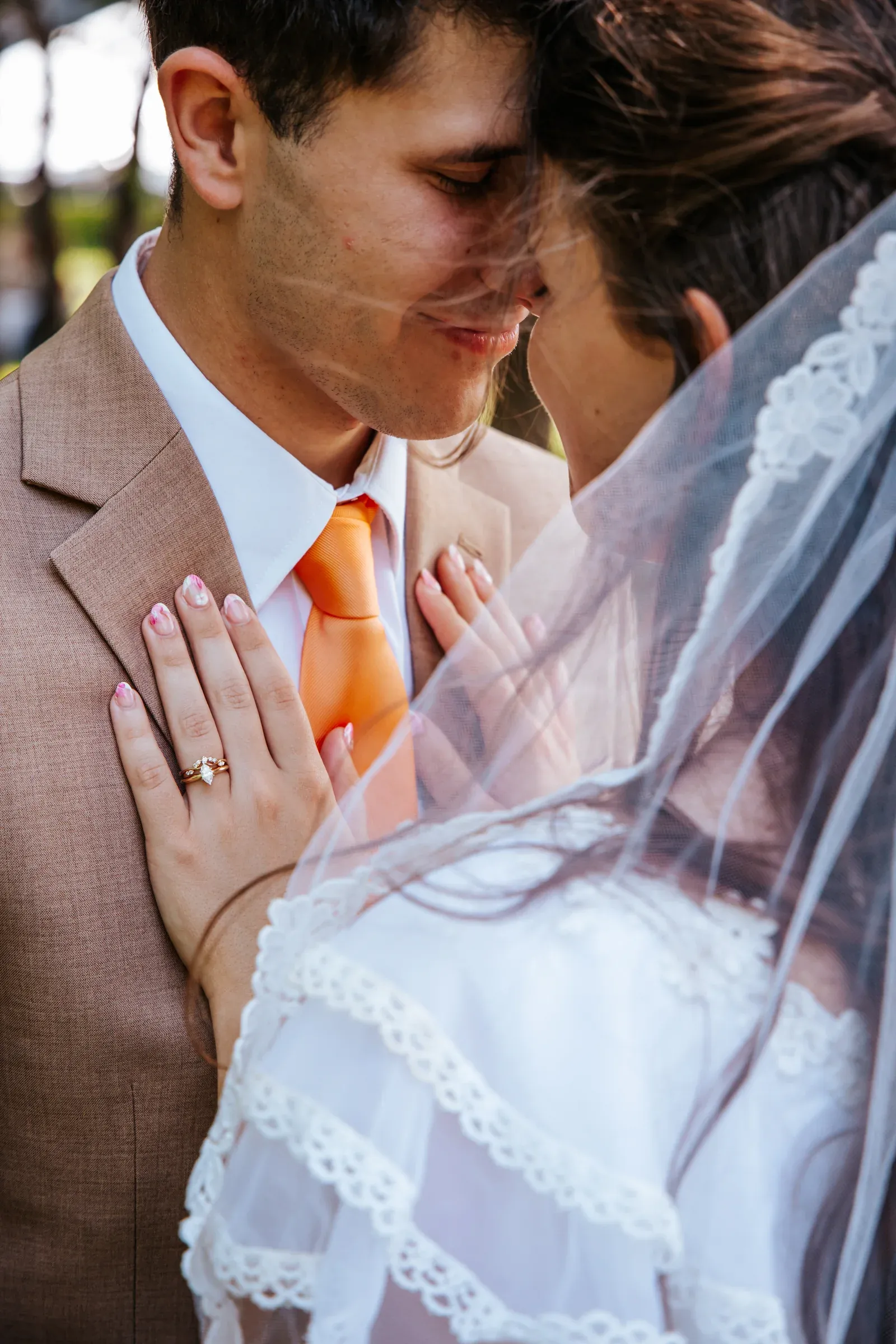 Newlyweds standing close together beneath a soft veil