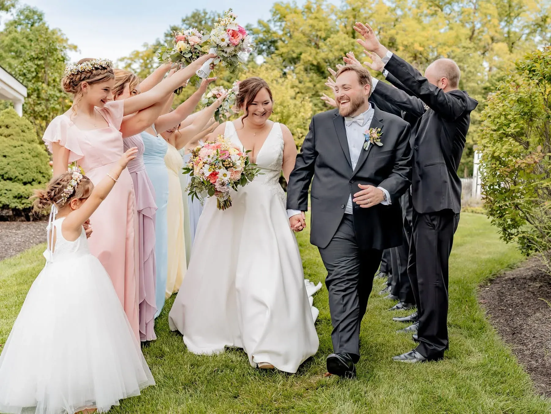 Wedding party raising their bouquets as the newlyweds walk through