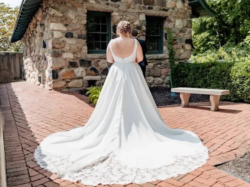 Bride showing the full train of her wedding dress beside a stone cottage